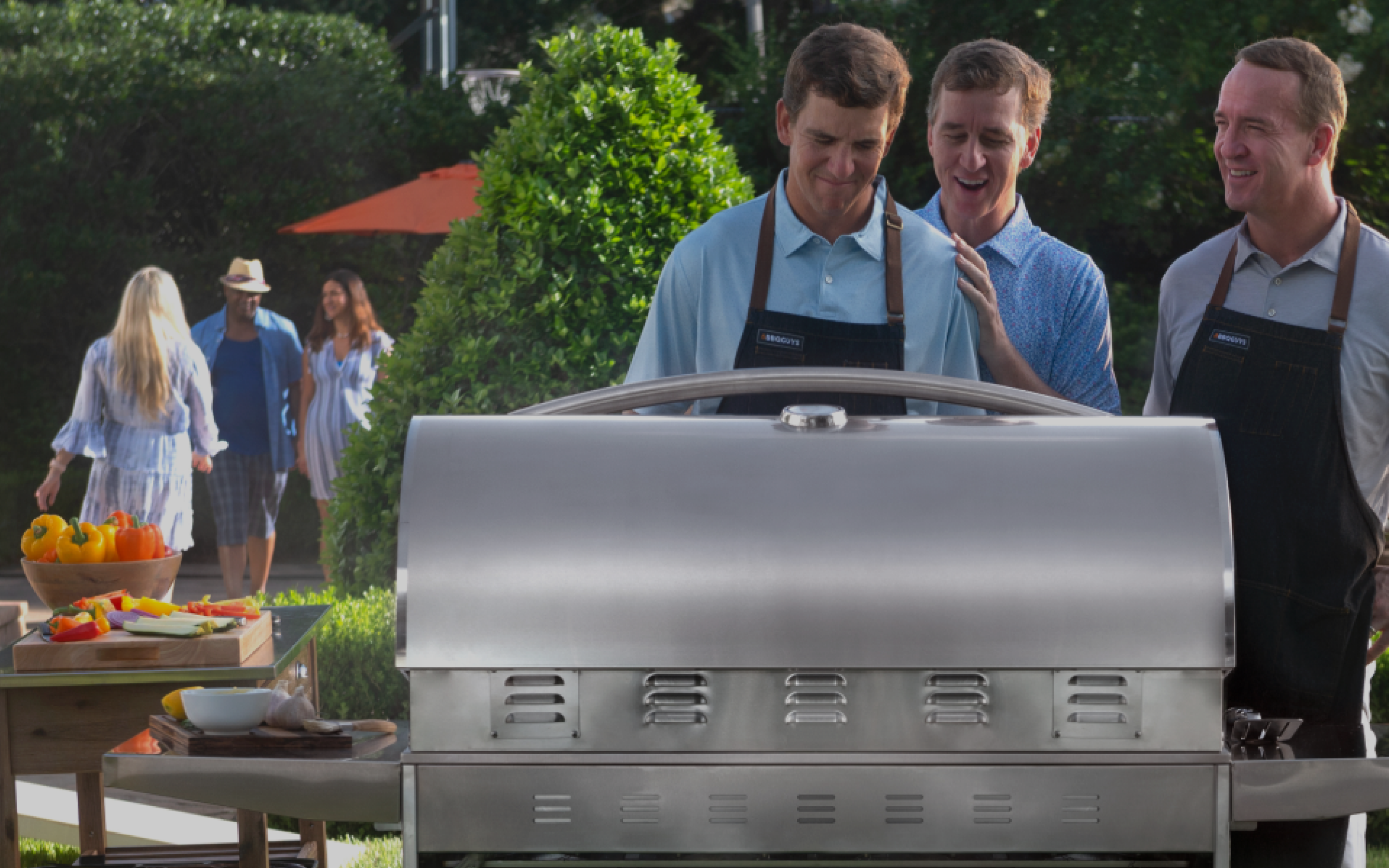 The Manning family standing over a grill.