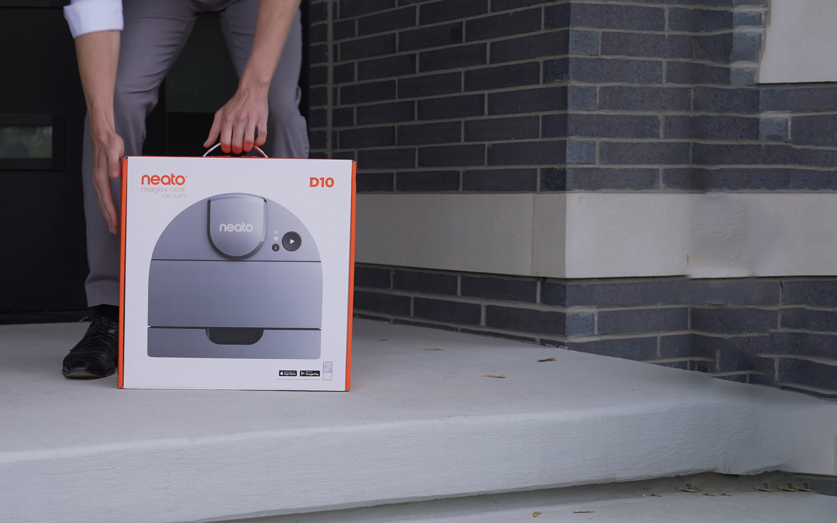 A man picking up a Neato Robotics vacuum in the packaging.