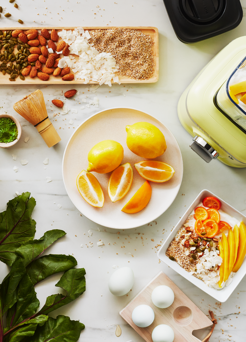 Sliced and whole lemons next to the base of a Kyoto Glow pale lime colored KitchenAid blender.