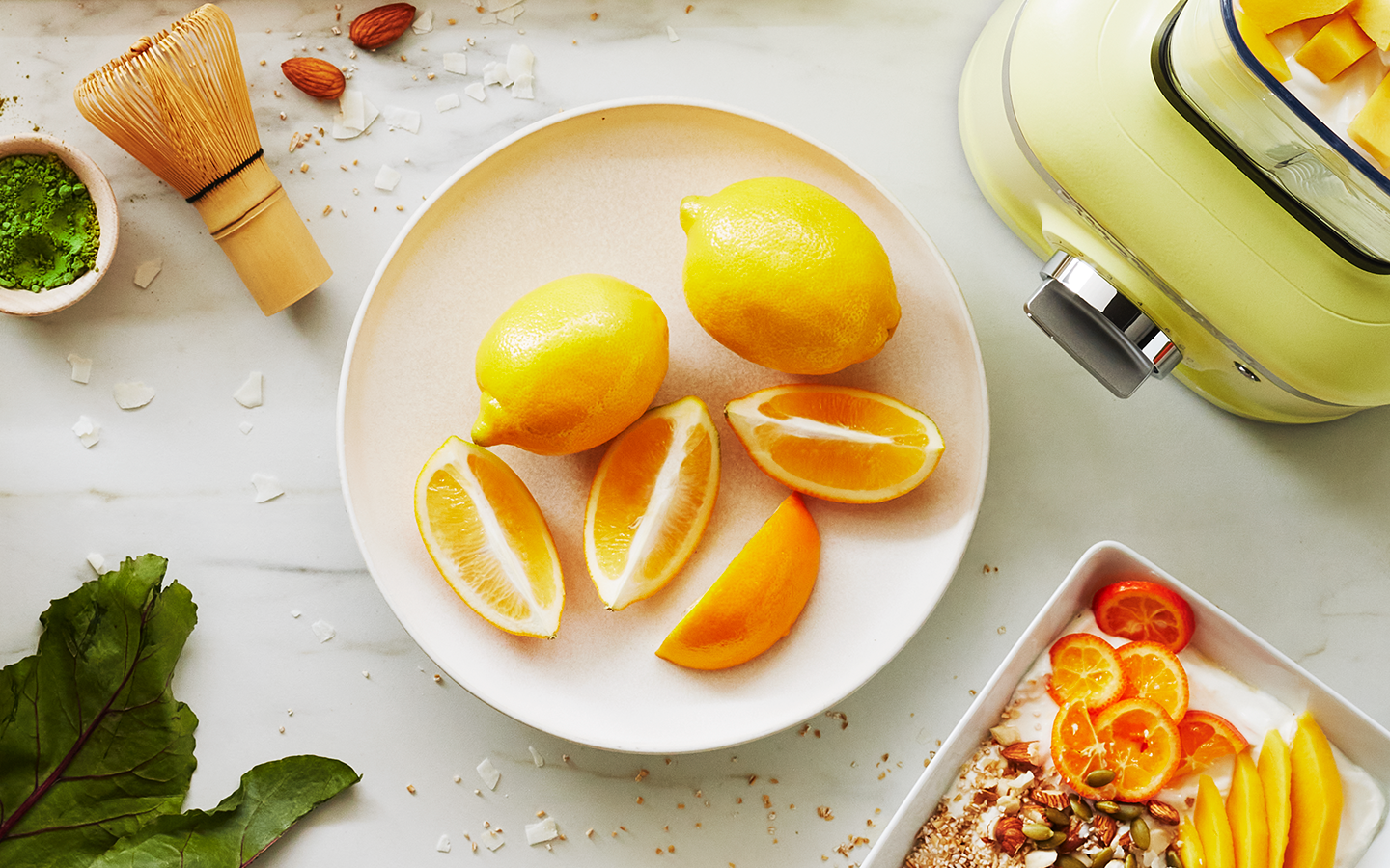 Sliced and whole lemons next to the base of a Kyoto Glow pale lime colored KitchenAid blender.