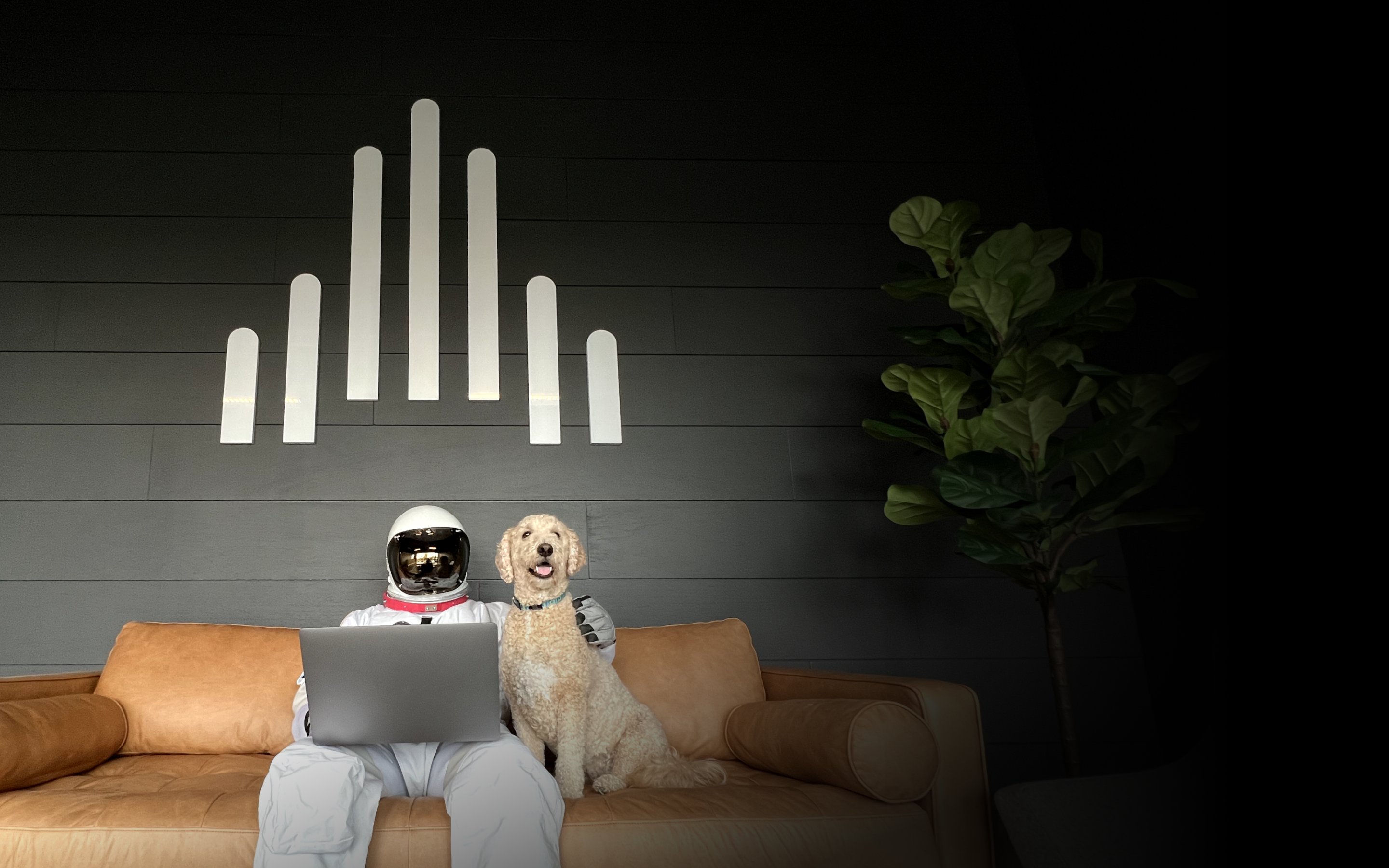 An astronaut with a laptop, sitting on a couch with a large dog.