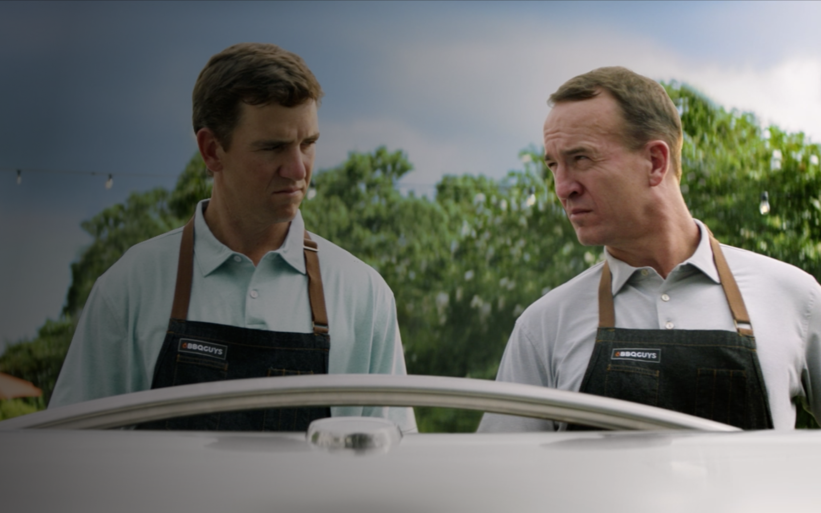 The Manning family standing over a grill.